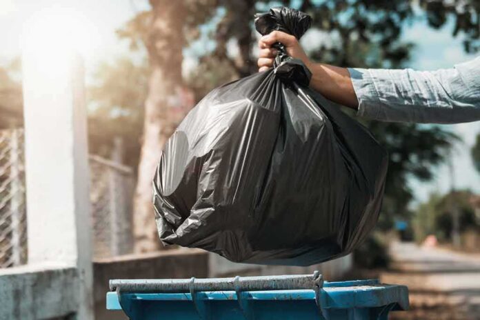 Hand dropping a black garbage bag into a blue bin