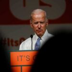 Gas Guzzlers Back? Biden’s EV Mandate OUT older man at a podium speaking on stage
