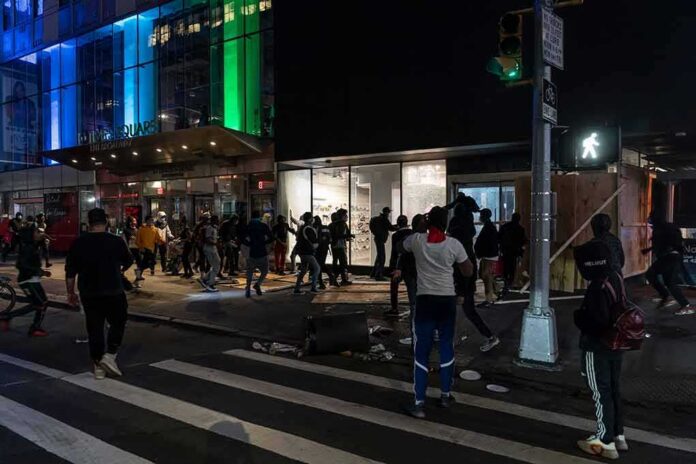 shutterstock_1747500134 Crowd outside a storefront at night with broken windows and debris
