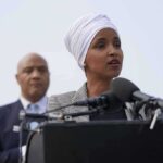 Ilhan Omar speaking at a podium with André Carson standing behind