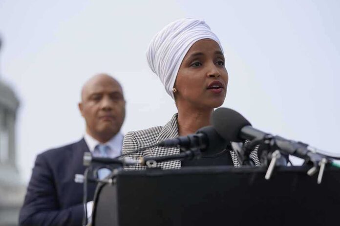 shutterstock_2012384414 Ilhan Omar speaking at a podium with André Carson standing behind