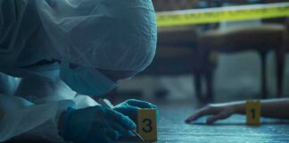 forensic investigator in protective suit examining crime scene markers
