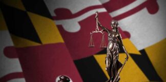 Lady Justice statue with gavel and book before a colorful flag backdrop