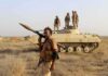 Soldier with RPG launcher walking past armored vehicle with troops
