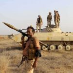 Soldier with RPG launcher walking past armored vehicle with troops