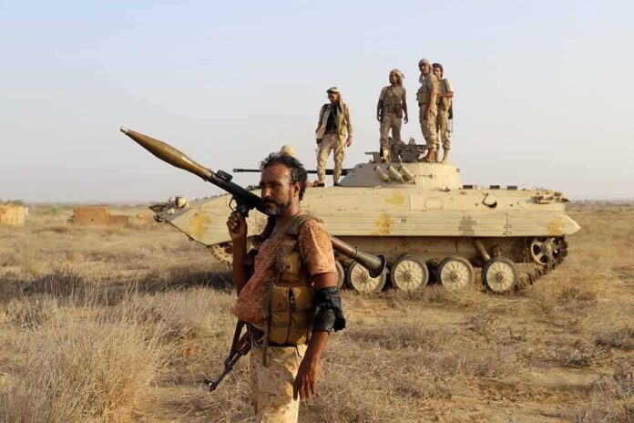 Soldier with RPG launcher walking past armored vehicle with troops