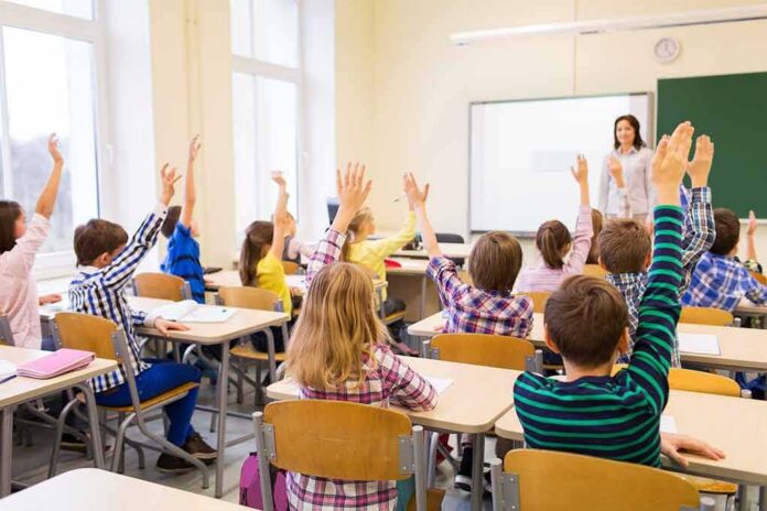 shutterstock_303888209 Students raise hands in a classroom while a teacher stands at the front