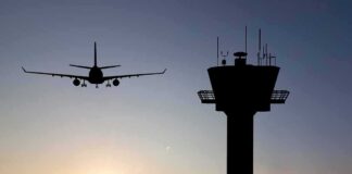 Airplane approaching runway near airport control tower at sunset