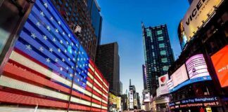 American flag LED display in a busy city square at dusk