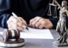 Defamation Playback – Online Outrage Meets Legal Brick Wall Judge writing at desk with gavel and Lady Justice statue