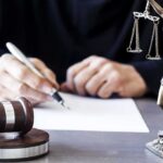 Defamation Playback – Online Outrage Meets Legal Brick Wall Judge writing at desk with gavel and Lady Justice statue