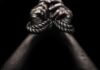 Hands bound with rope against a dark background