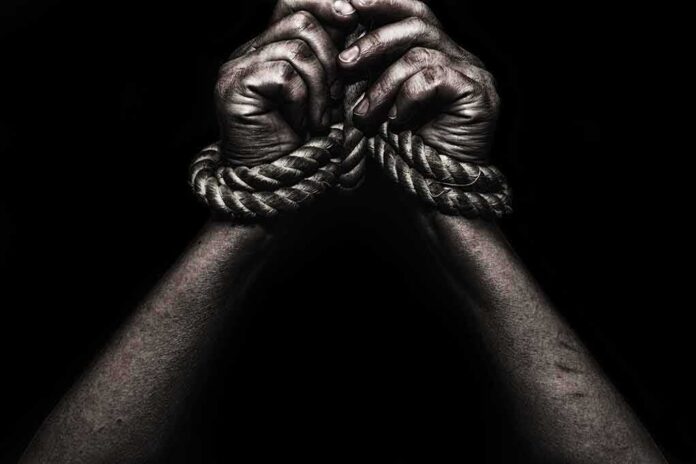 shutterstock_608866748 Hands bound with rope against a dark background
