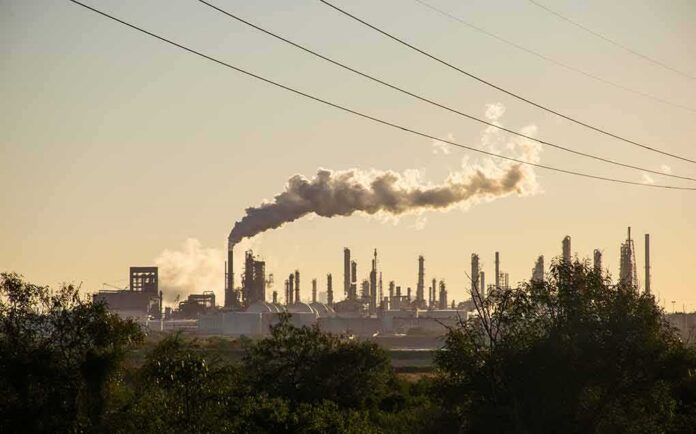 Industrial refinery with smokestack emitting plume at sunset