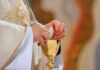 Priest holding a communion wafer over a gold chalice