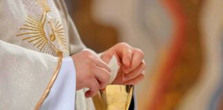 Priest holding a communion wafer over a gold chalice