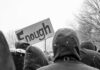 Shot From Behind? DHS Story Wobbles crowd in winter coats at a protest holding a sign