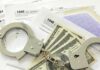 Tax Refund Rampage: Father – Son Plot Drains Millions? Handcuffs on tax forms with cash