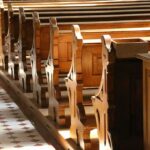 Worship Lines Blurred – Catholics Furious wooden church pews in sunlight