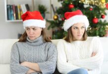 Two women in Santa hats sitting with arms crossed on a couch