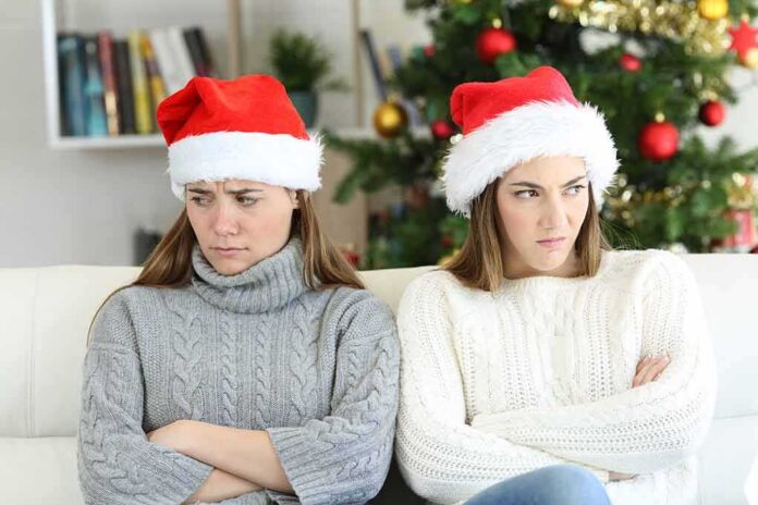 Two women in Santa hats sitting with arms crossed on a couch