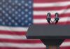 Stunned Crowd As Candidate Ducks Iran Call Podium with microphones in front of a blurred American flag