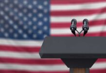 Podium with microphones in front of a blurred American flag