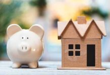 California Housing Math Just Broke Piggy bank beside cardboard house model on a table
