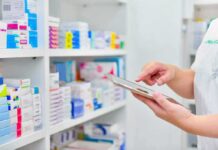 Reckless or Relief? HHS Quietly Opens Peptide Backdoor Pharmacist using a tablet in front of stocked pharmacy shelves