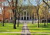 Donor Power Fight Erupts at Harvard Students walking on a university campus with autumn trees and a historic building in the background