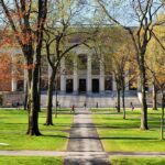 Donor Power Fight Erupts at Harvard Students walking on a university campus with autumn trees and a historic building in the background