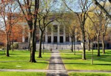 Donor Power Fight Erupts at Harvard Students walking on a university campus with autumn trees and a historic building in the background