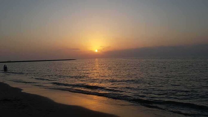 shutterstock_1954311112 Sunset over calm sea with gentle waves on a sandy beach